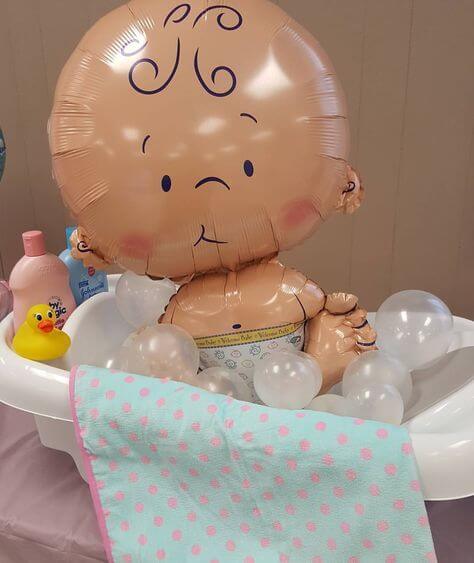 Baby shaped mylar balloon sitting in a toy bathtub with bubles made of small clear latex balloons.