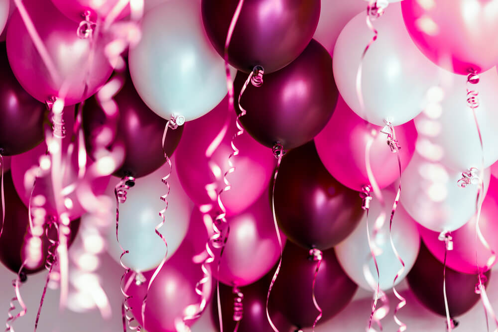 Pink, purple and white balloons with ribbons hanging from ceiling