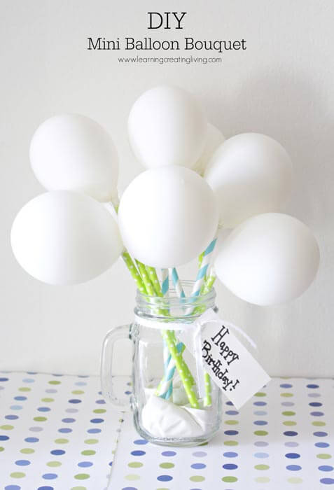 Several white latex balloons attached to green and blue straws and arranged in a mason jar like a flower bouquet.
