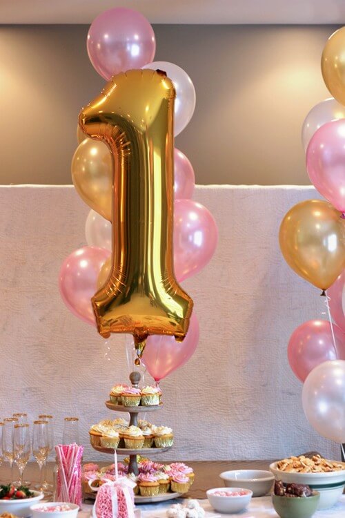 Gold number one mylar balloon and a bouquet of pink, pearl and gold latex balloons as cake table decoration for a first birthday party.