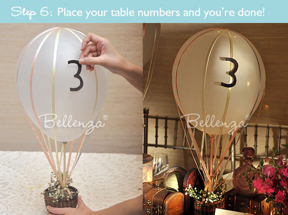 Two hot air balloon centerpieces in white and ochre, with balloon sticks (no helium) and small wicker baskets filled with tiny white flowers.