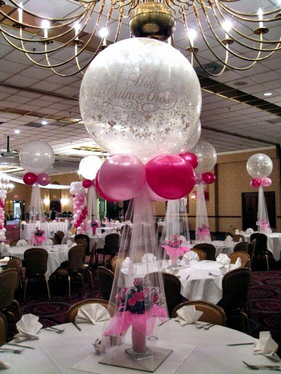 Pink and white balloon centerpiece for Quinceanera party, with tulle strings and a flower bouquet as part of the table base.