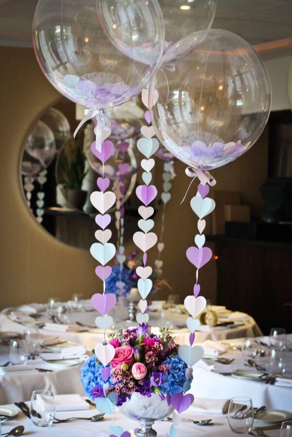 Wedding balloon centerpiece with three clear deco bubbles, using pastel colored paper hearts as confetti and for the strings, attached to a flower base.