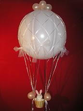 Hot air balloon centerpiece with 36 inch white balloon, wicker basket and a stuffed bunny in front of dark red background.
