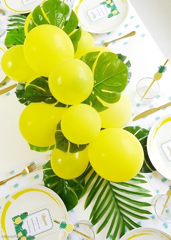 Tablescape made of bright yellow latex balloons in different sizes, monstera leaves and palm fronds.