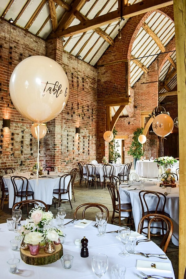 Wedding table balloon centerpieces displaying the table numbers in a rustic barn setting.